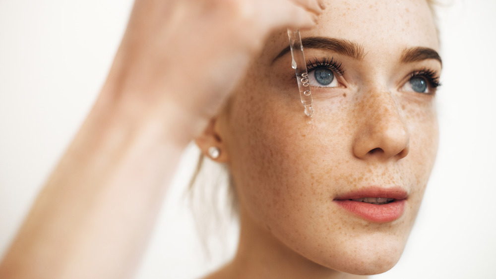 Woman with freckles applying serum 