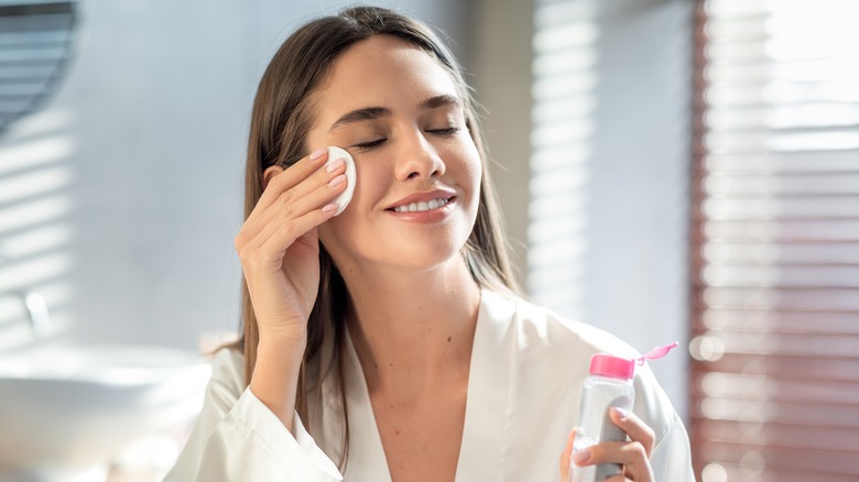 Woman puts toner on her face with cotton pad