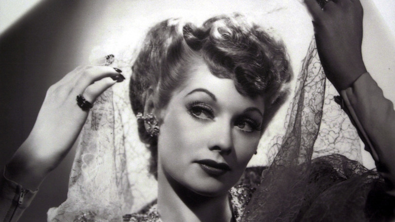 Lucille Ball smiles softly as she drapes lace around her head, Black and white photo