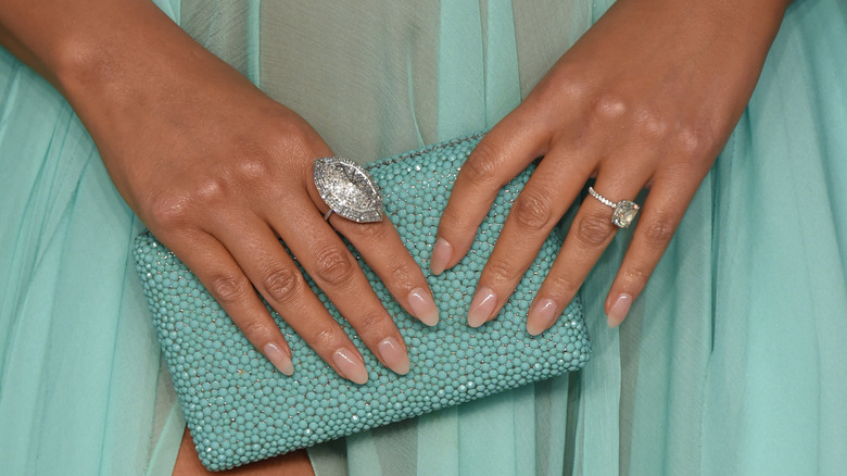 Chrissy Teigen clutches her purse, showcasing a nude manicure.