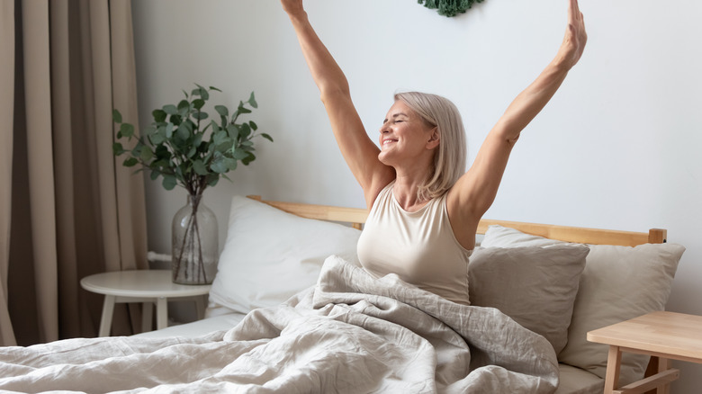 A woman waking up in bed and stretching while smiling 