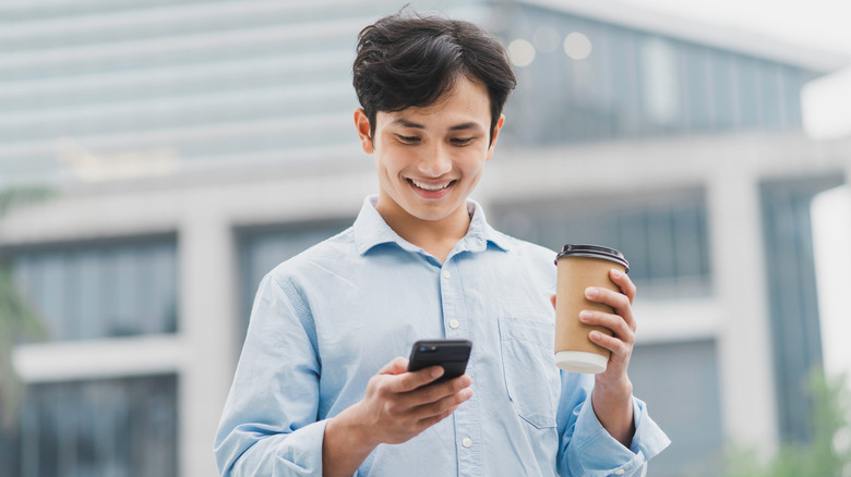 person holding coffee and looking at phone