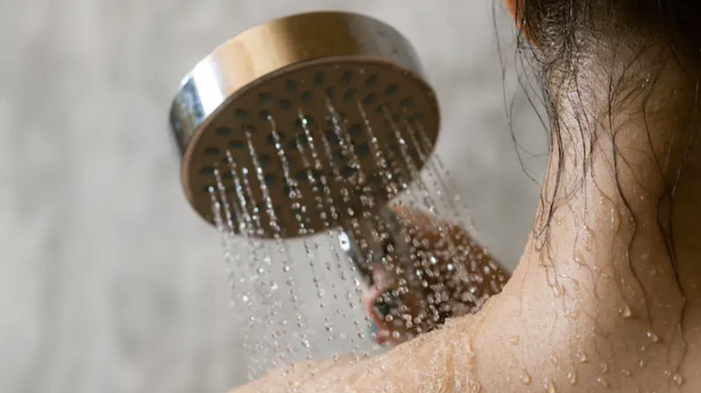 Woman uses shower head to clean shoulder