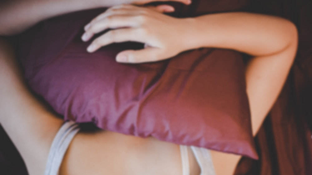 Woman on a bed with a pillow over her head.