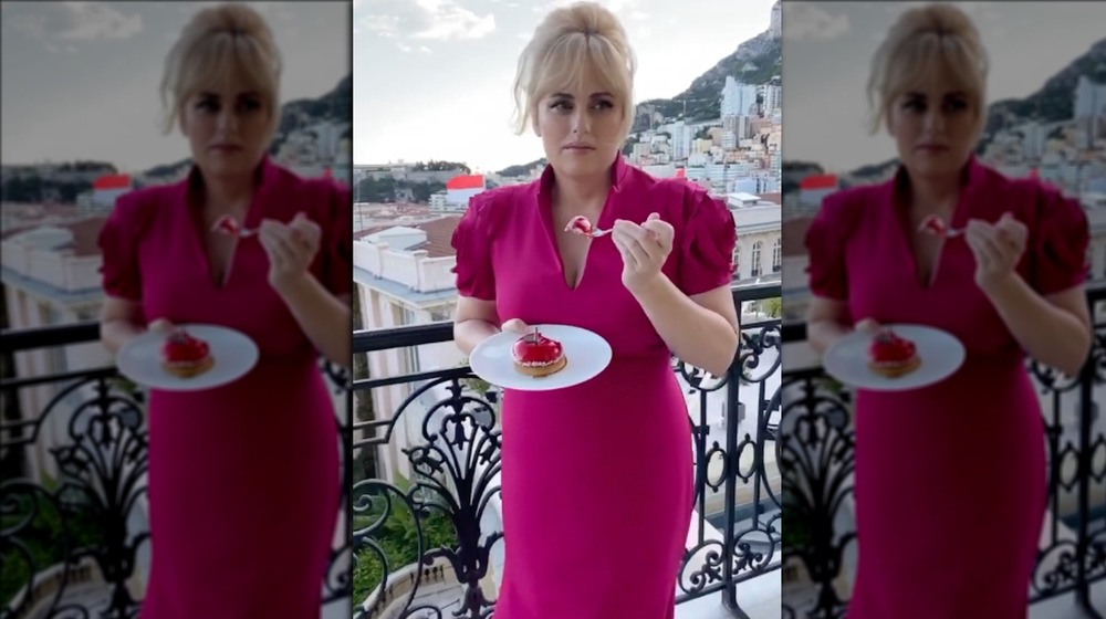 Rebel Wilson eating cake on a balcony