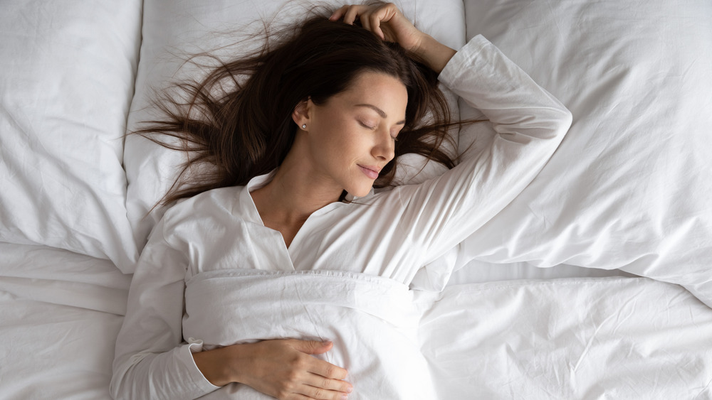 A woman happily sleeping on her back in white bedding 