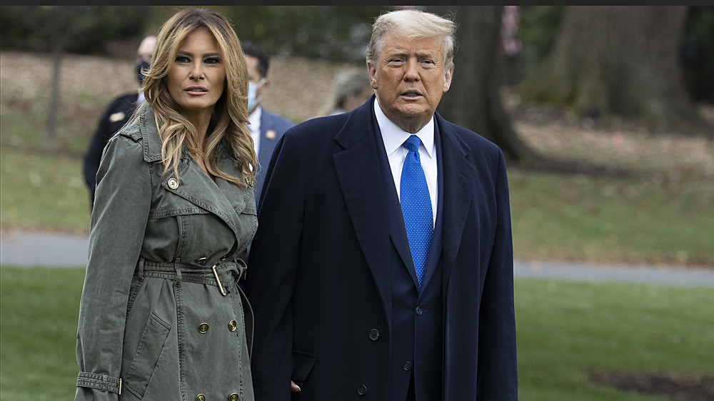 Melania Trump in trench coat with hair down and Donald Trump in blue suit and coat