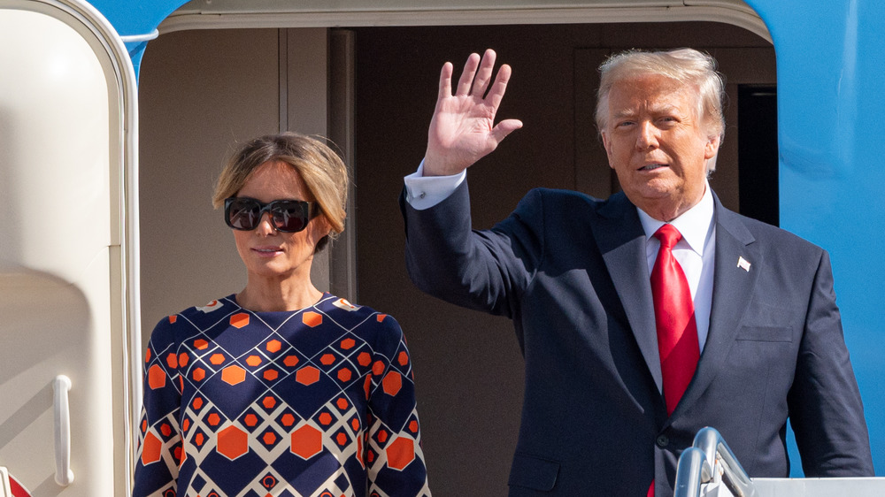 Donald Trump waving Melania Trump in dark sunglasses and bright patterned dress