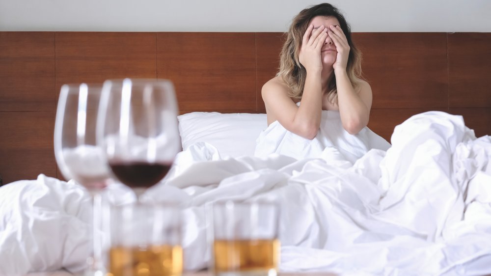 woman in bed hungover with drinks in view 