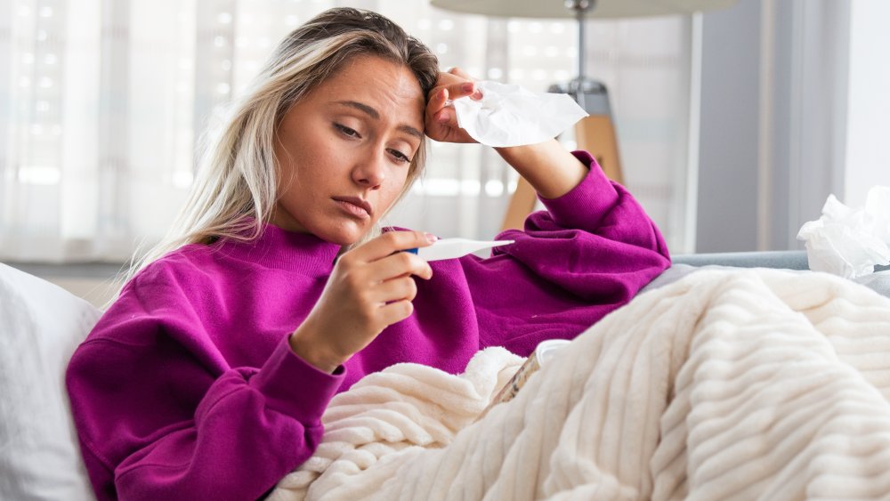 Woman sitting on couch holding thermomenter