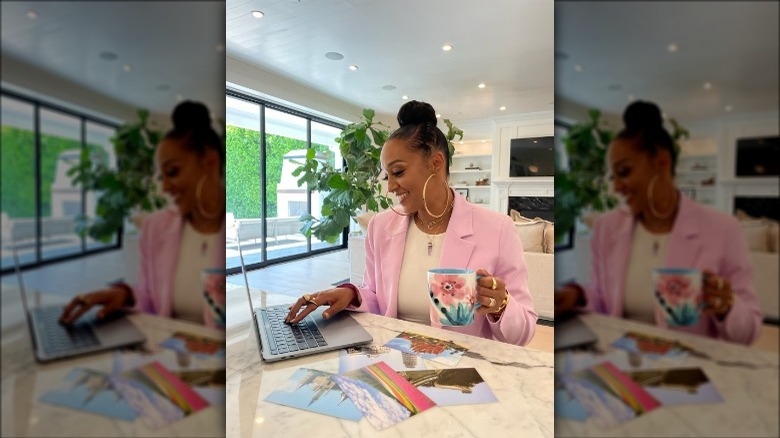 Tia Mowry working on laptop with cup of coffee in her hand