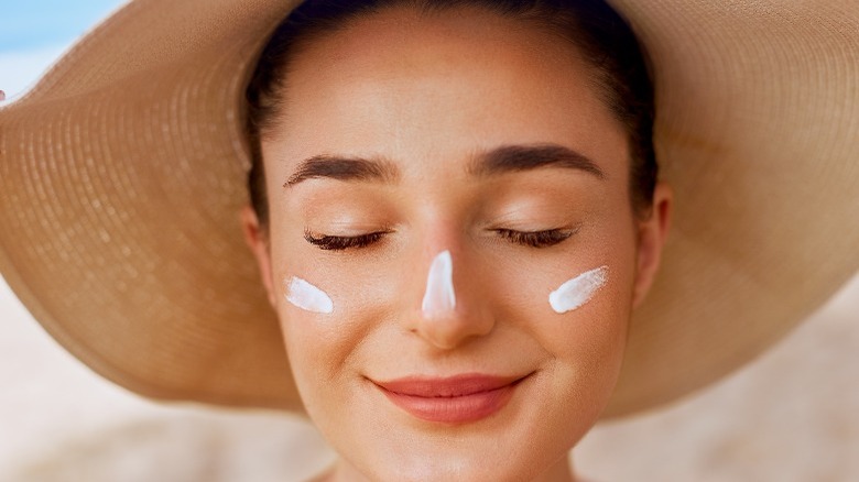 woman with sunscreen on nose and cheeks wearing wide-brim hat