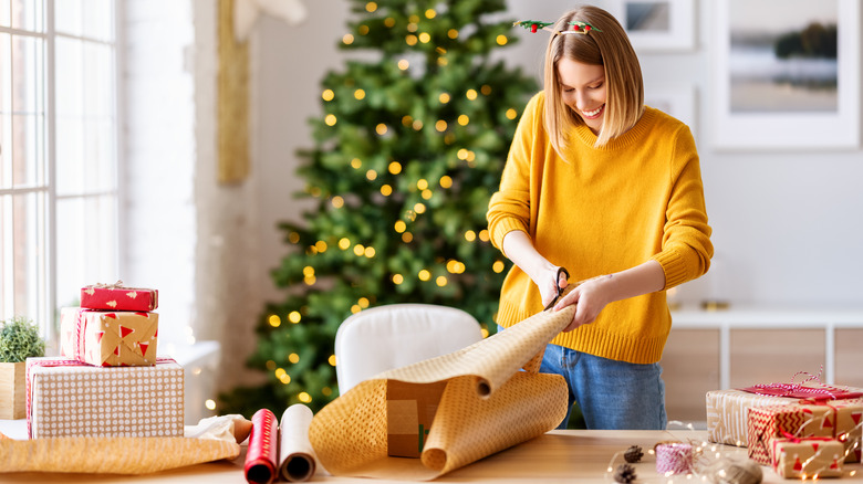 Woman standing in front of a Christmas tree wrapping a present