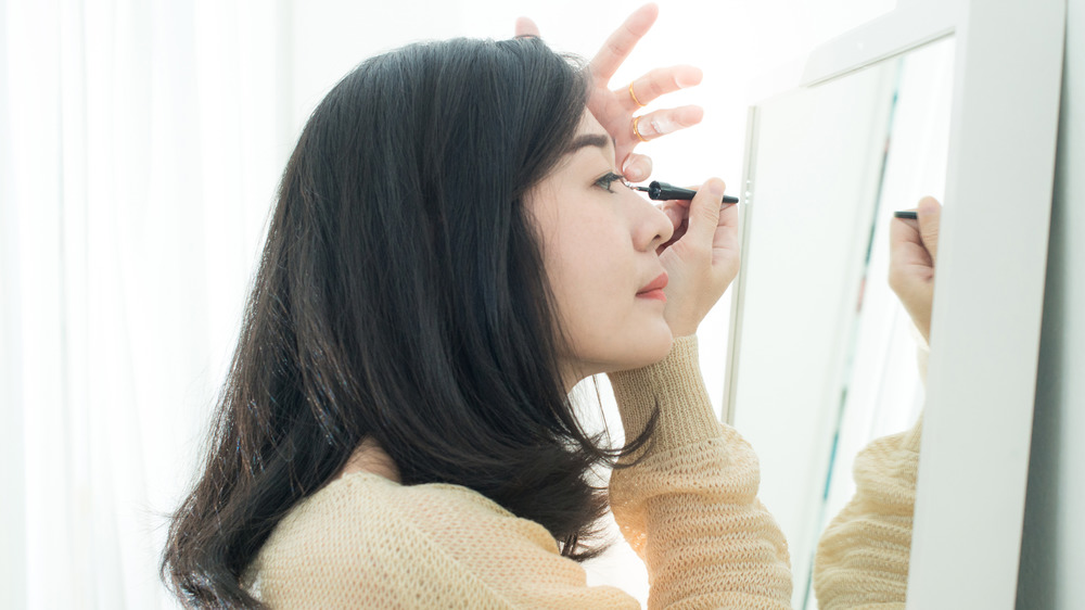 A woman applying eye makeup in the mirror 