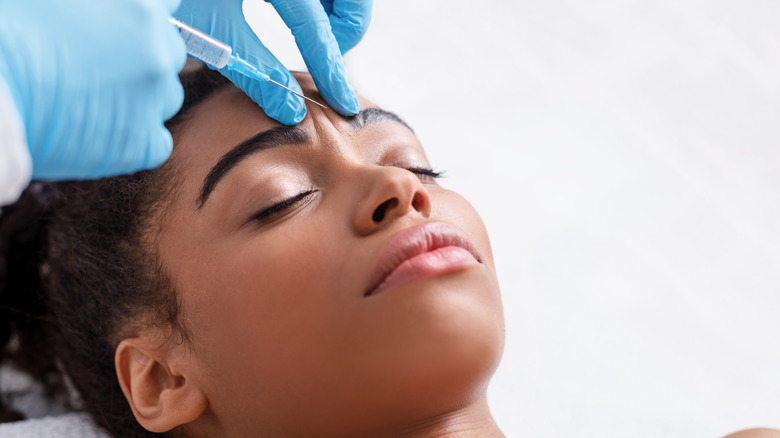 Black woman receiving facial filler in between brows