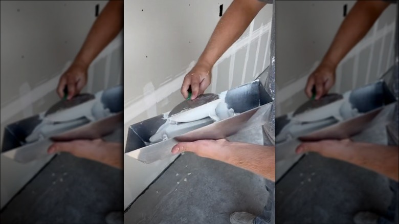 Construction worker loading his spatula with mud before applying it to drywall.