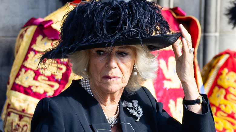 Queen Camilla touching the black hat on her head