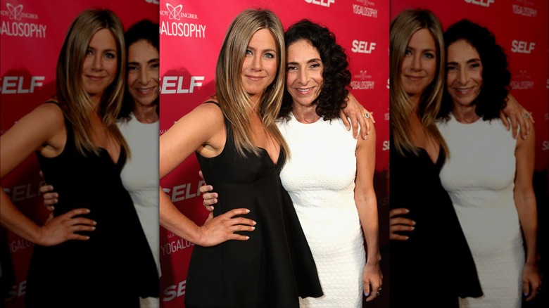 Jennifer Aniston posing with arm around yoga instructor Mandy Ingber in aubergine frilled dress