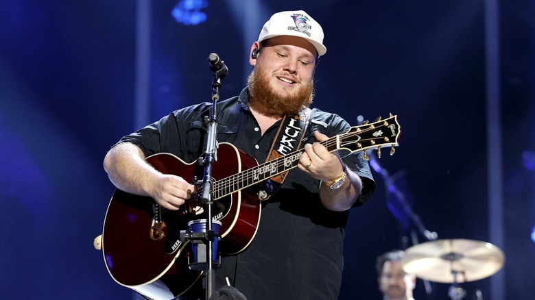 Luke Combs playing guitar, smiling