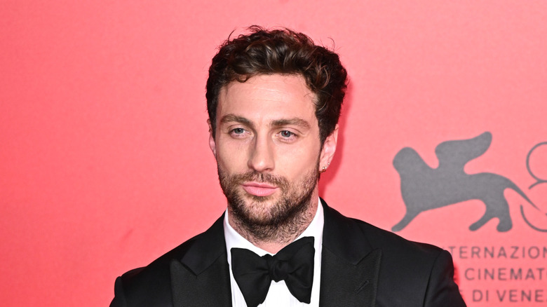 Aaron Taylor-Johnson in front of red background in black tuxedo