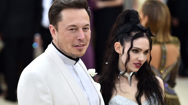 Elon Musk in a white tuxedo and Grimes in a white dress, on the red carpet at the Met Gala