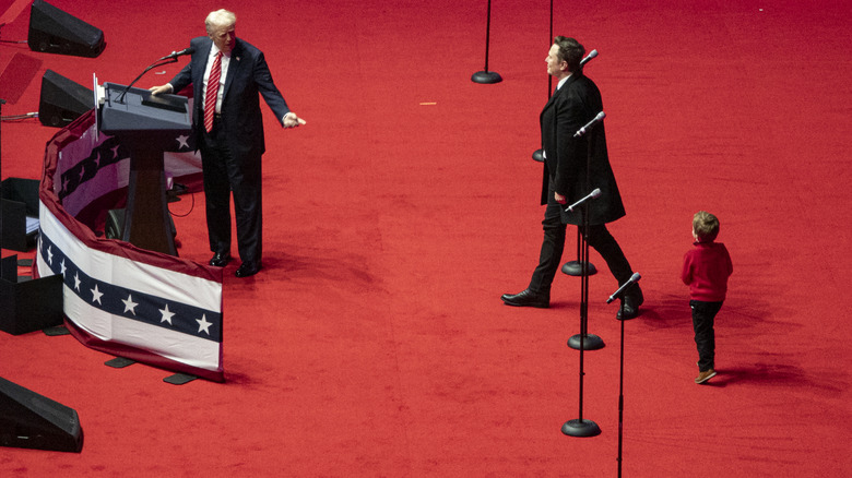 Donald Trump, Elon Musk with his fists raised, and X on stage at a Trump rally