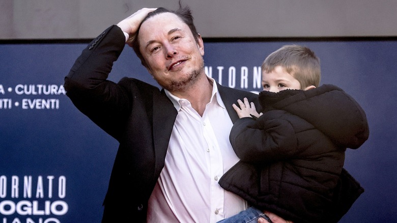 Elon Musk pushing his hair back while holding his son X