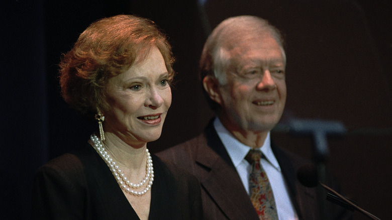 Rosalynn and Jimmy Carter smiling next to each other in front of microphone