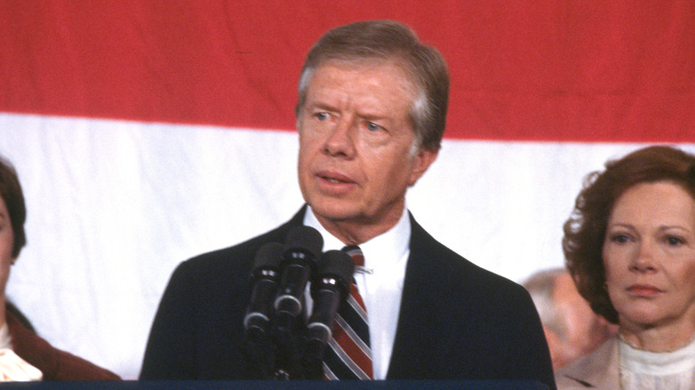 Jimmy Carter speaking at podium with Rosalynn Carter watching