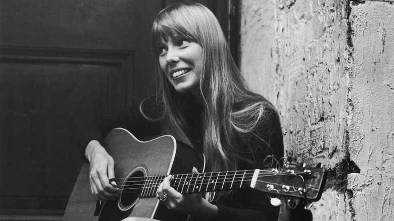 Young Joni Mitchell smiling and playing guitar