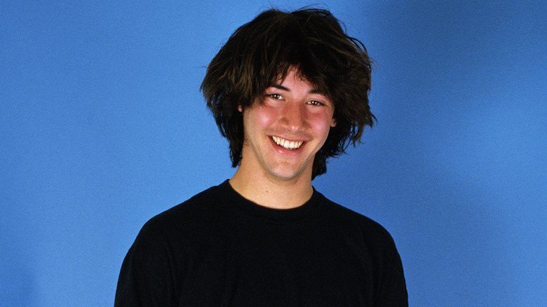 A young Keanu Reeves smiling against blue background