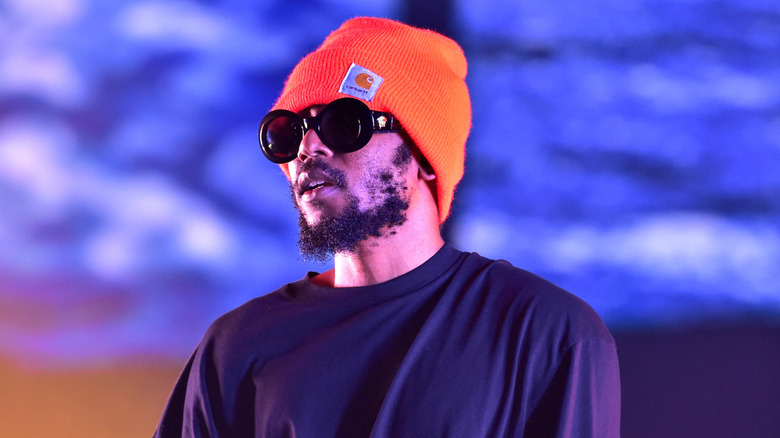 Kendrick Lamar on stage wearing sunglasses and an orange hat