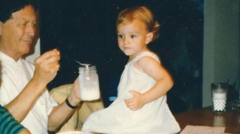 Leighton Meester as a toddler sitting on a table wearing a white dress