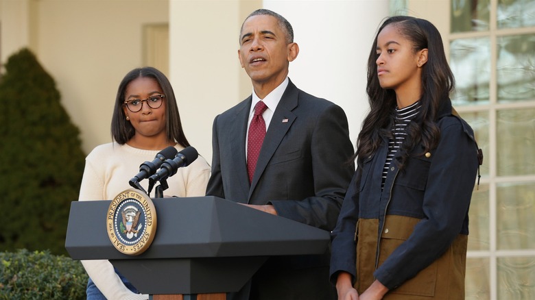 Sasha Obama and Malia Obama standing with Barack Obama