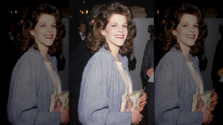 Gilda Radner smiling in purple jacket holding clutch bag