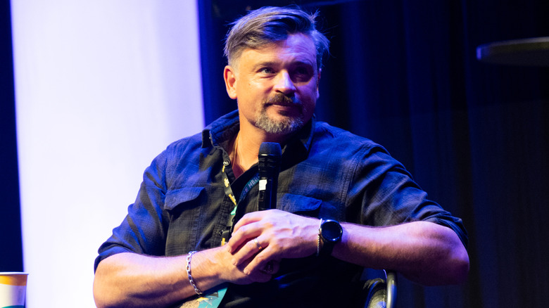 Tom Welling holding a microphone while sitting on stage