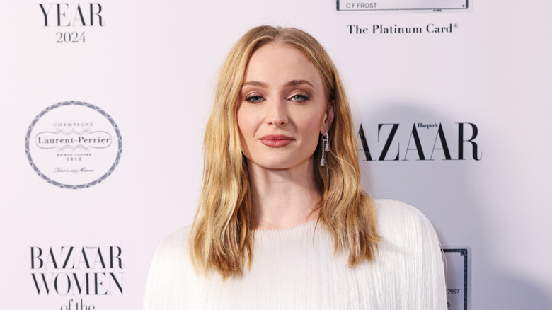 Sophie Turner smiling and posing at an event in a white shirt