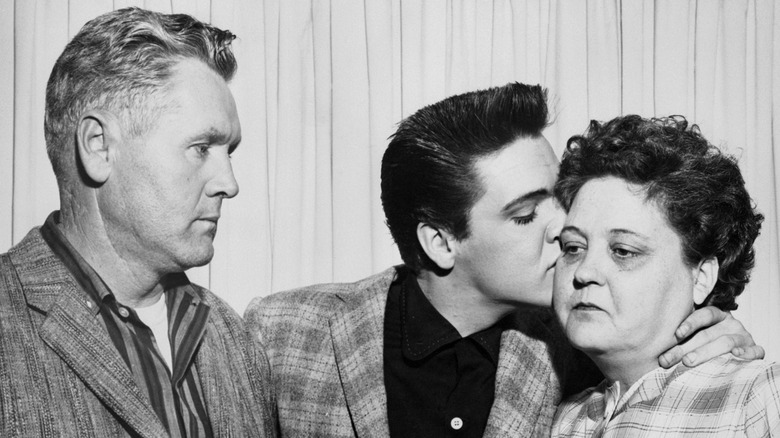 Elvis Presley kissing his mother on the cheek while his father watches