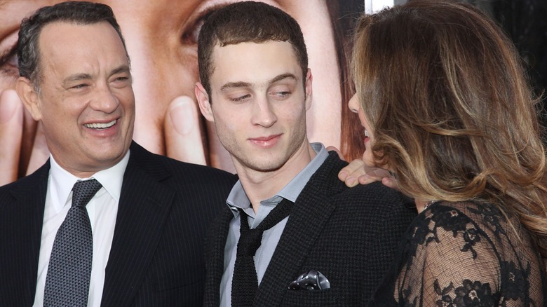 Chet Hanks in a suit and tie looking at his mom Rita Wilson and standing beside his smiling dad Tom Hanks