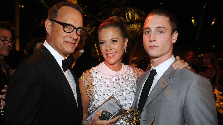 Tom Hanks in a tux and glasses, Rita Wilson in White dress with crystals, and Chet Hanks in gray suit