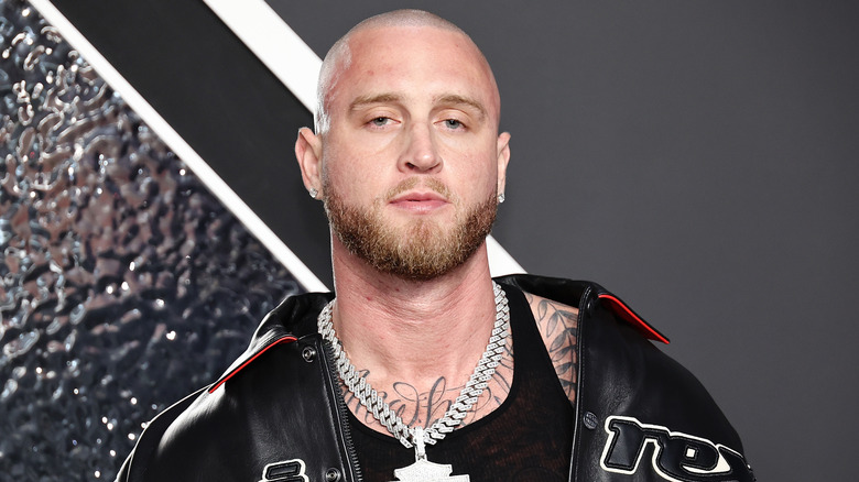 Chet Hanks with shaved head, beard, wearing leather jacket and large silver necklace