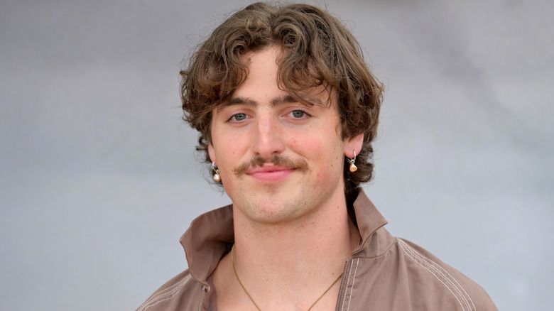 Benson Boone smiles while wearing a brown shirt with a popped collar