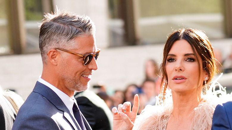 Bryan Randall smiling and Sandra Bullock raising her hand