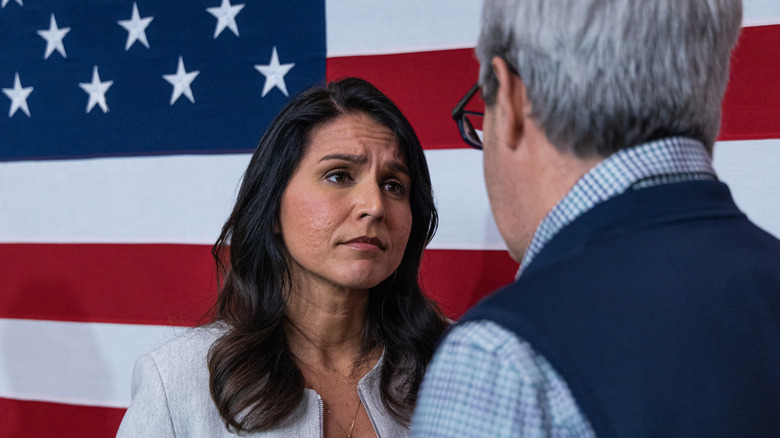 Tulsi Gabbard looking serious in front of American flag