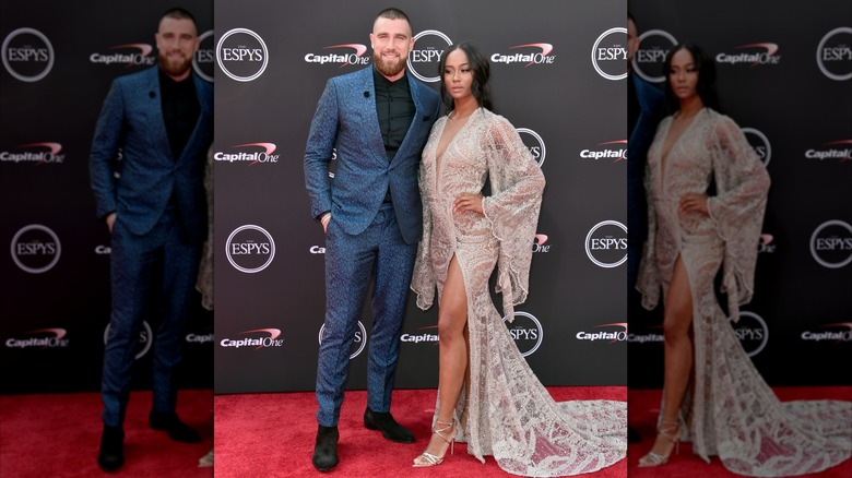 Travis Kelce and Kayla Nicole posing on the red carpet, he in a blue suit and smiling, she looking serious in a lace dress.