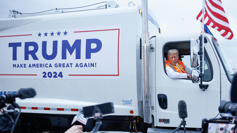 Donald Trump in branded garbage truck speaking to reporters