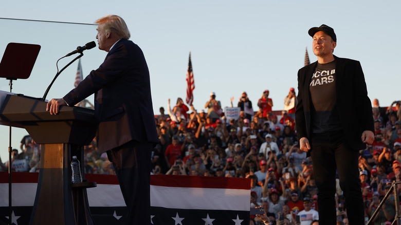 Elon Musk standing behind Donald Trump at a campaign event