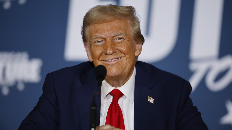 Donald Trump seated smiling in front of microphone