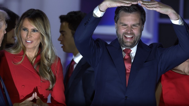 Melania Trump talking to Donald Trump while JD Vance holds arms up in an 'O' shape