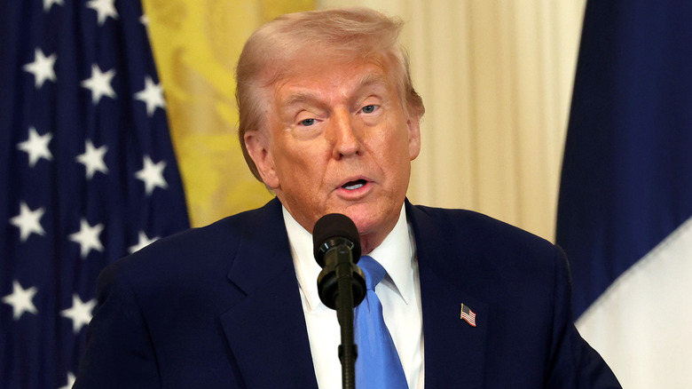 Donald Trump speaking on a podium with the American flag behind him